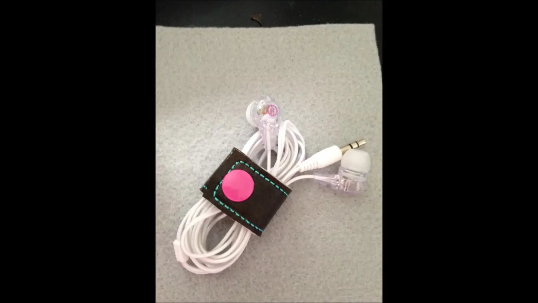 A finished brown vinyl cord keeper with pink snaps wrapped neatly around white earbuds.