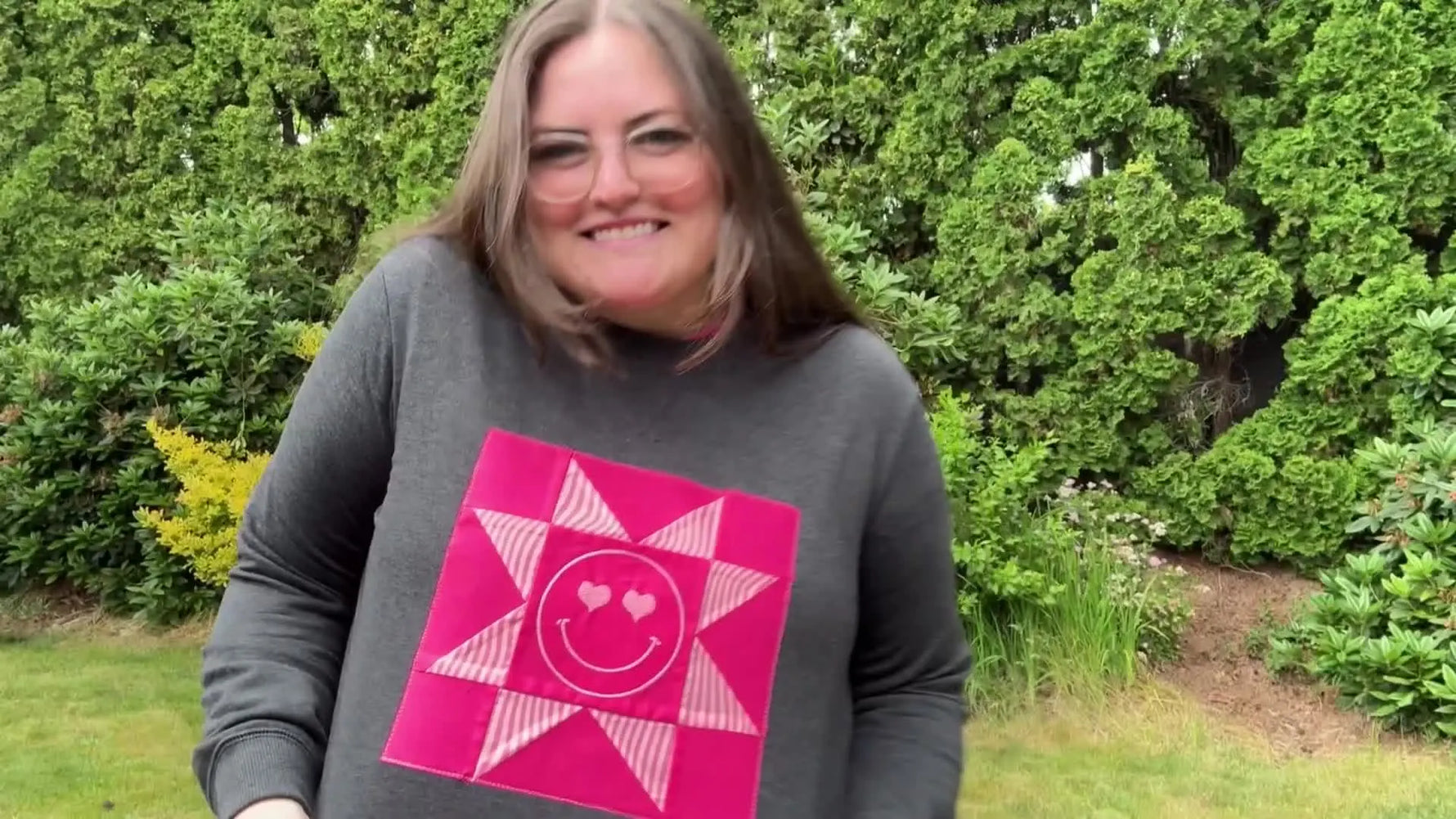 The finished embroidered quilt block sweatshirt is shown worn outdoors, highlighting the centered Sawtooth Star block with the stitched smiley face.
