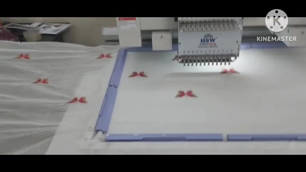A single-head industrial embroidery machine stitches a butterfly motif on a white saree held flat by purple clamping bars.