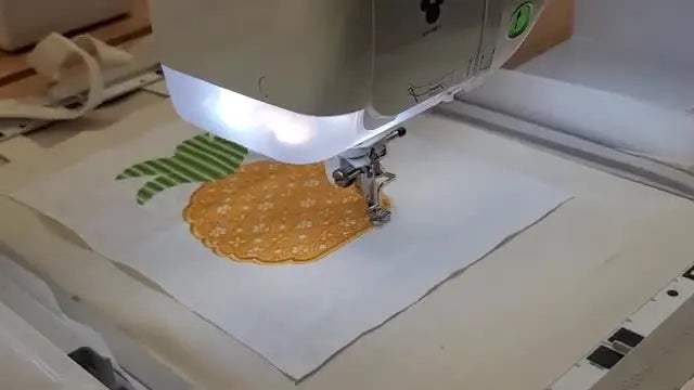 A close-up of the machine stitching the pineapple’s detailed gold fill, showing clean applique edges and stable fabric control.