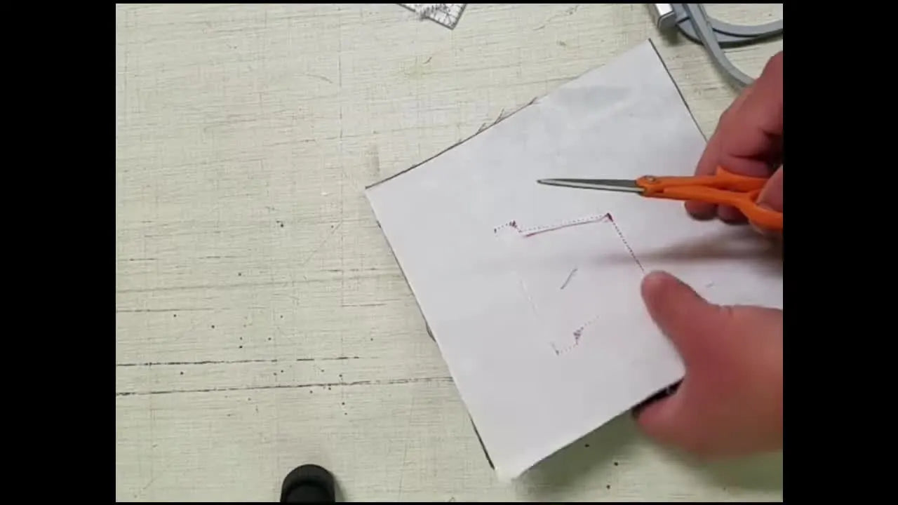Close-up of orange-handled scissors cutting directly on the stitched outline to create a perfectly sized clay pot appliqué edge.