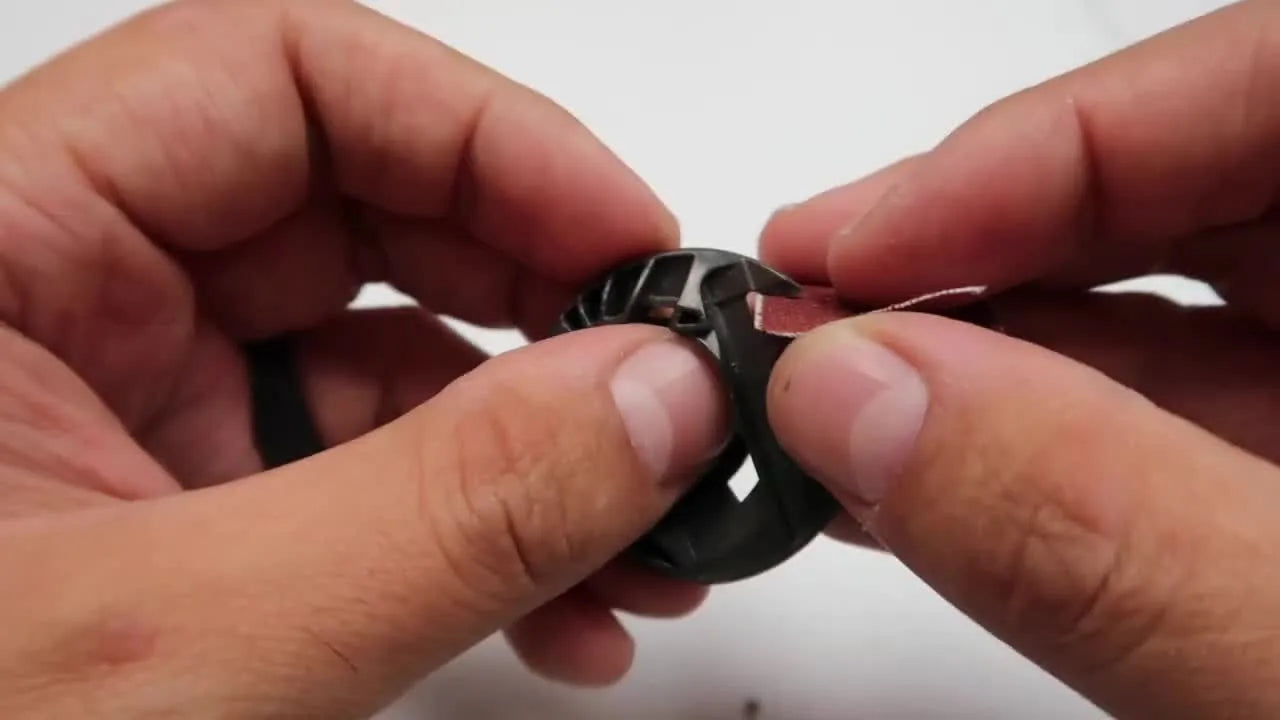 Hands use a small folded piece of sandpaper to smooth a nick on a plastic bobbin case for an emergency, get-you-through-the-order fix.