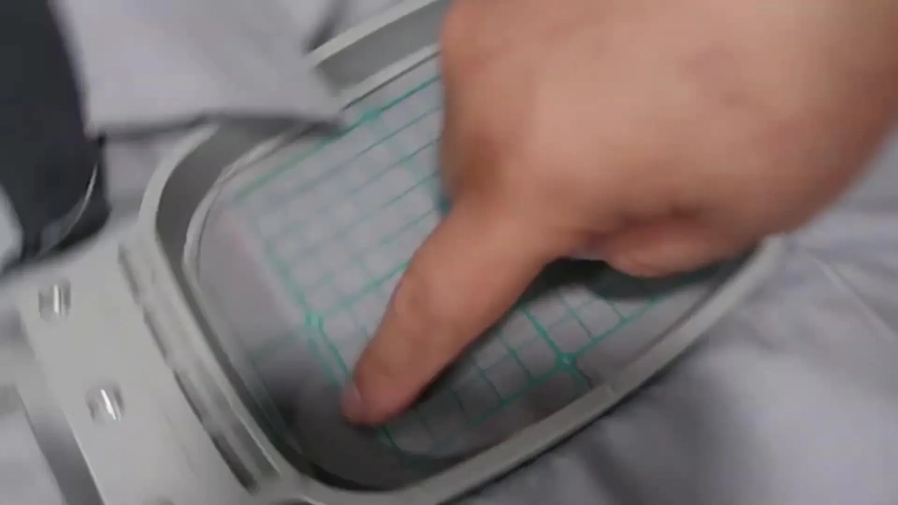 A close-up of a magnetic hoop grid being aligned to a shirt pocket edge and a marked centerline for precise logo placement.