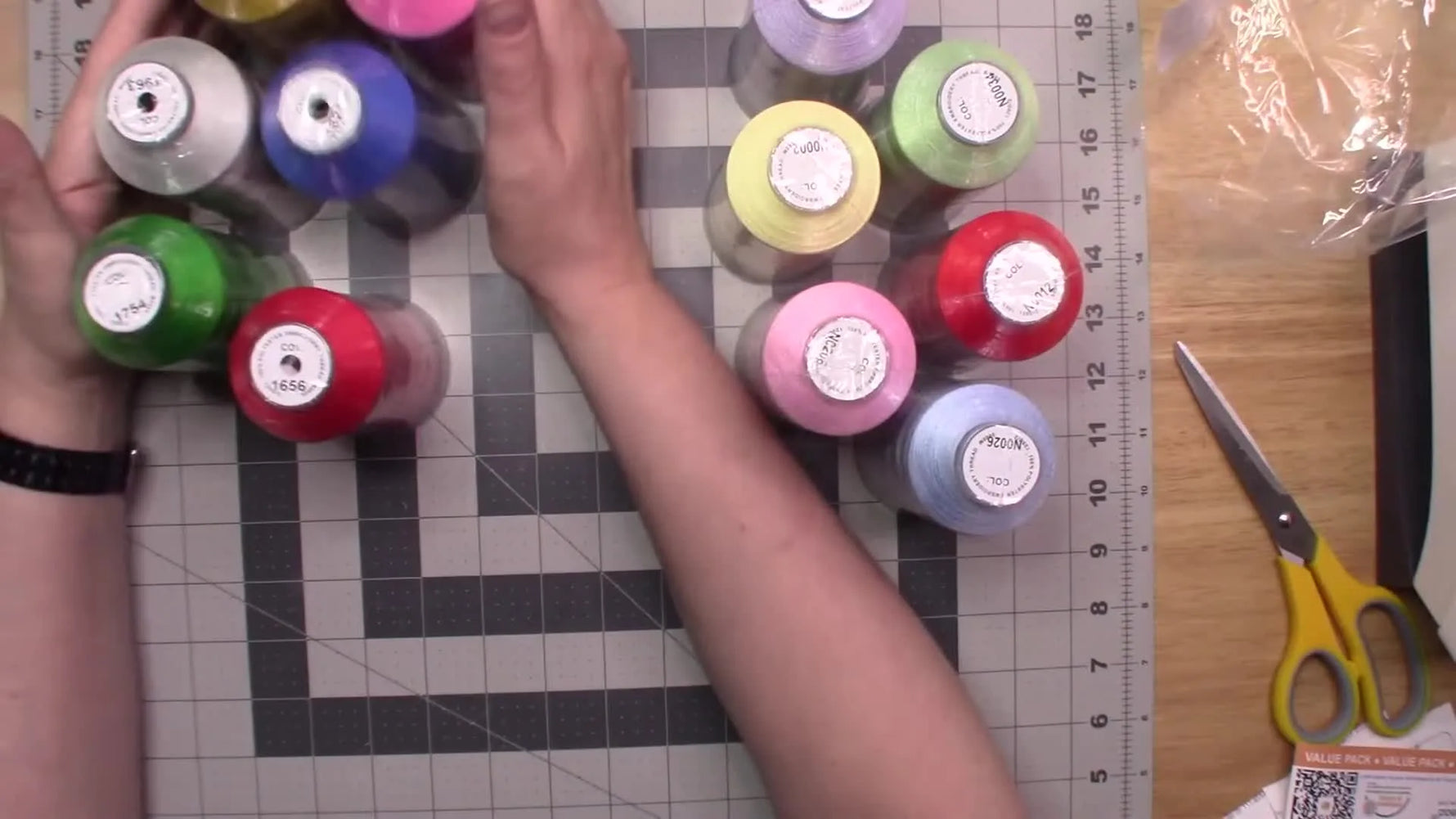 Twelve large embroidery thread cones are laid out on a cutting mat in two coordinated color groups for quick comparison and planning.