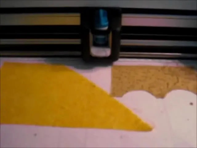 A close-up shows a pre-cut yellow duck appliqué being placed precisely inside the stitched placement line in an embroidery hoop.