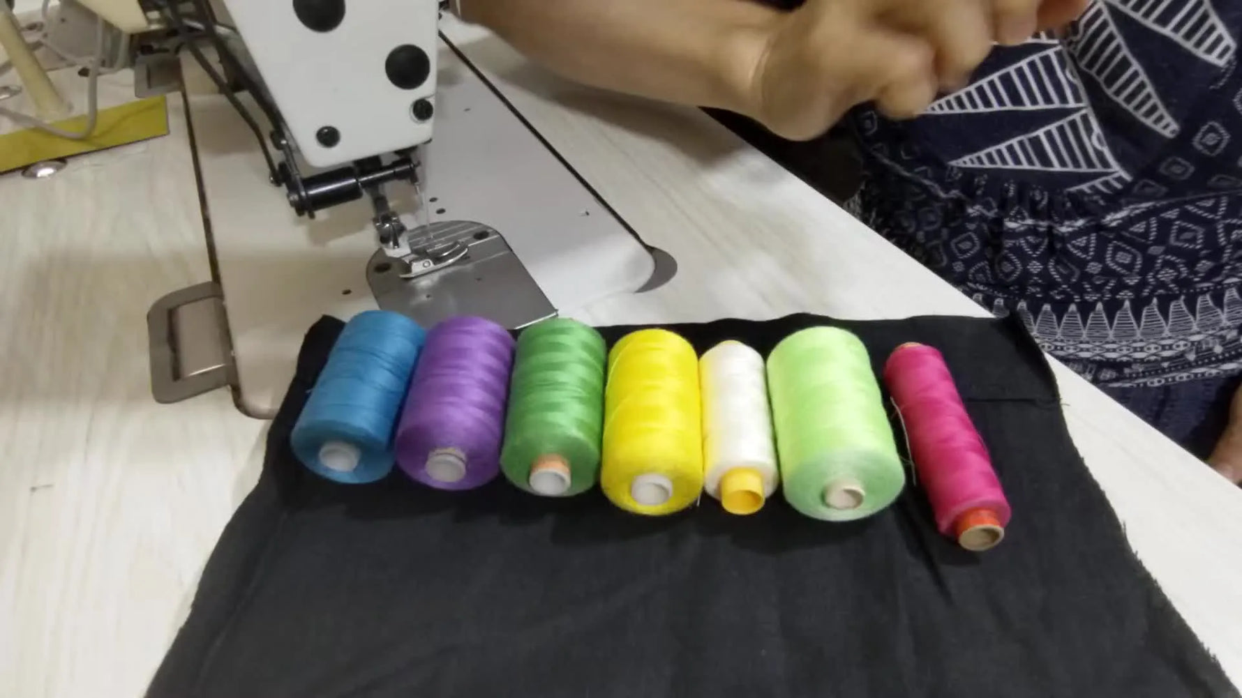 Collection of colorful thread spools lined up on black fabric next to a sewing machine.