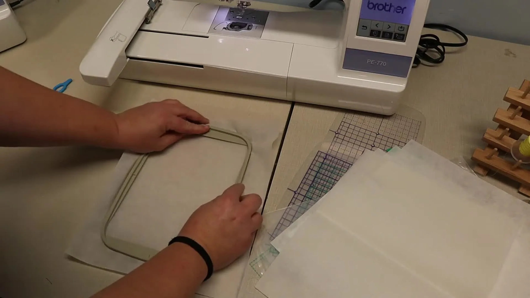 Hands press the inner ring into the outer ring to secure a stabilizer sheet in a 5x7 hoop before tightening the screw.