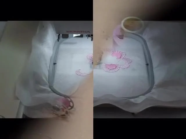 A close-up of an embroidery machine stitching a pink freestanding lace flower onto white water-soluble stabilizer.