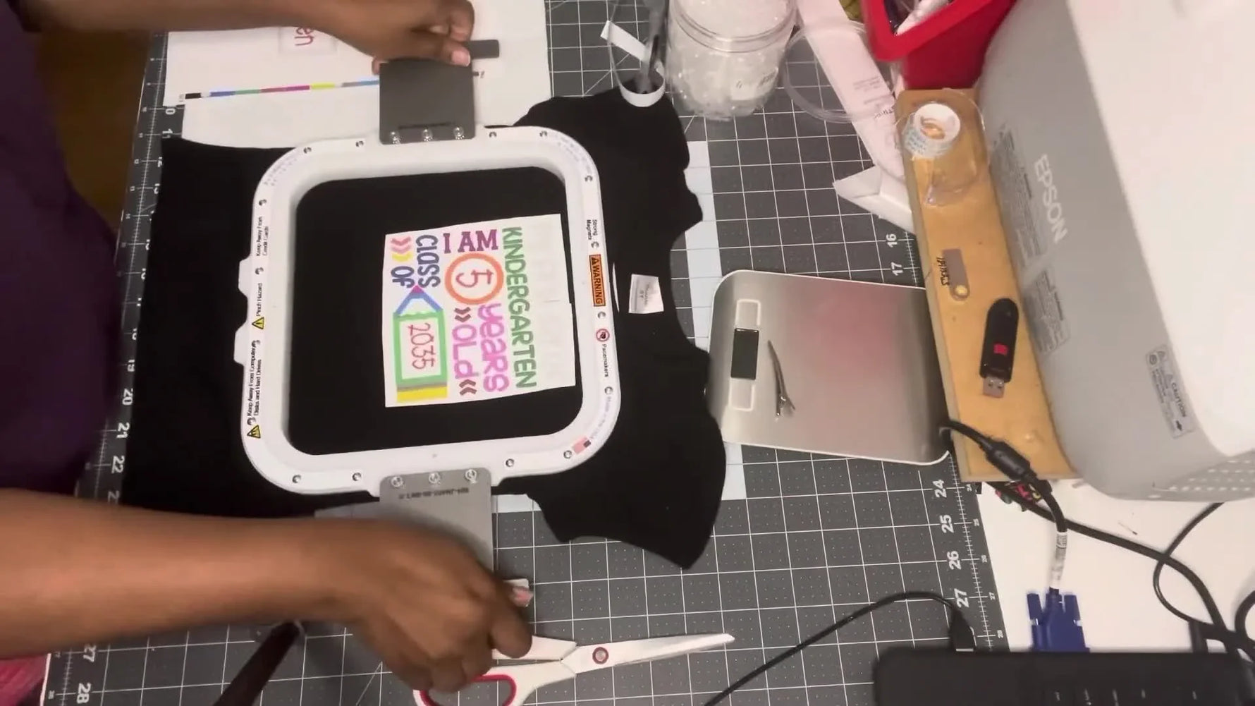 A magnetic hoop snaps shut over a small black kids’ t-shirt, locking placement in before stitching begins.