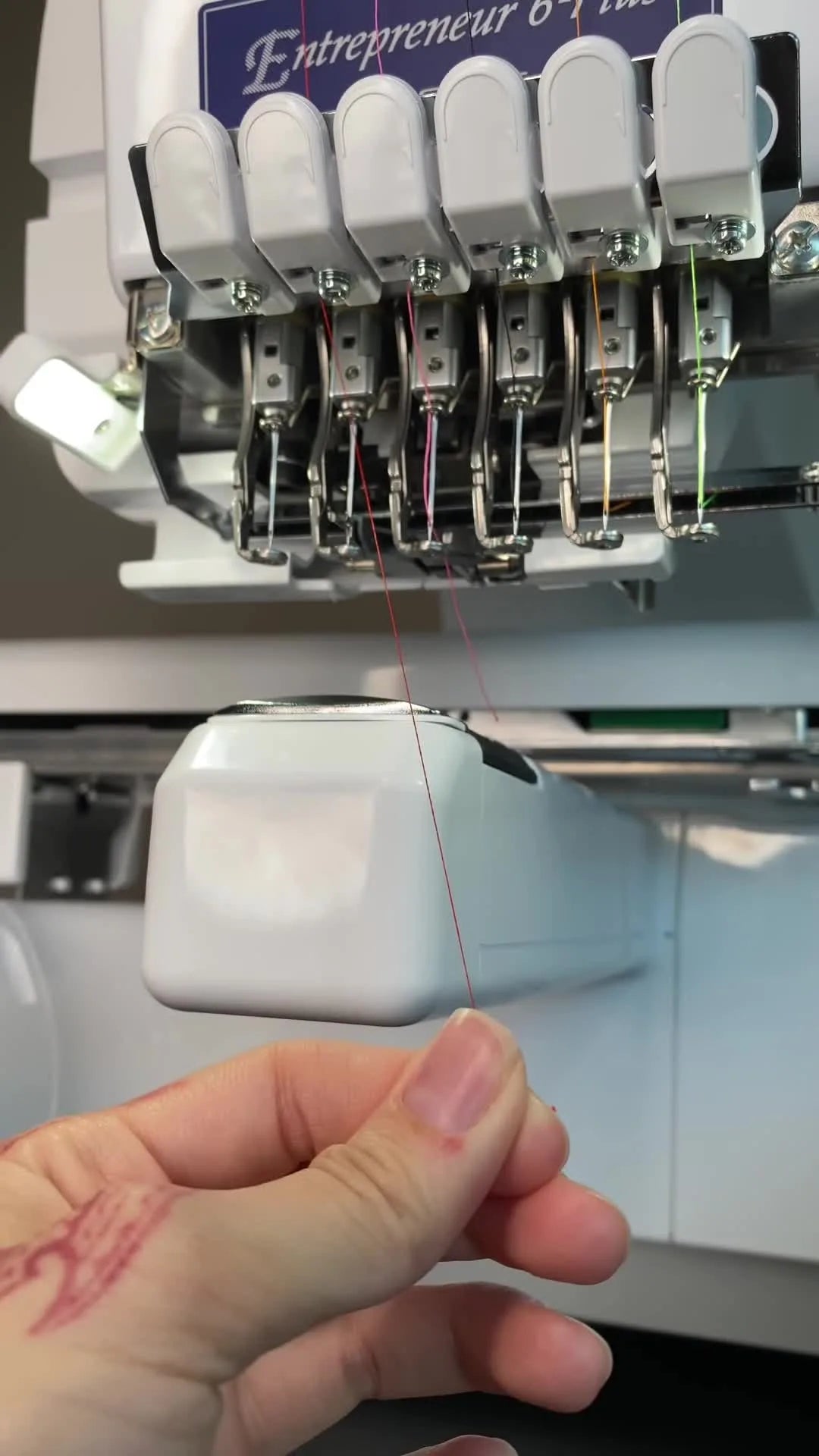 Close-up of the Brother PR670E automatic threading hooks extended around the needle as the thread is being wrapped for auto-threading.