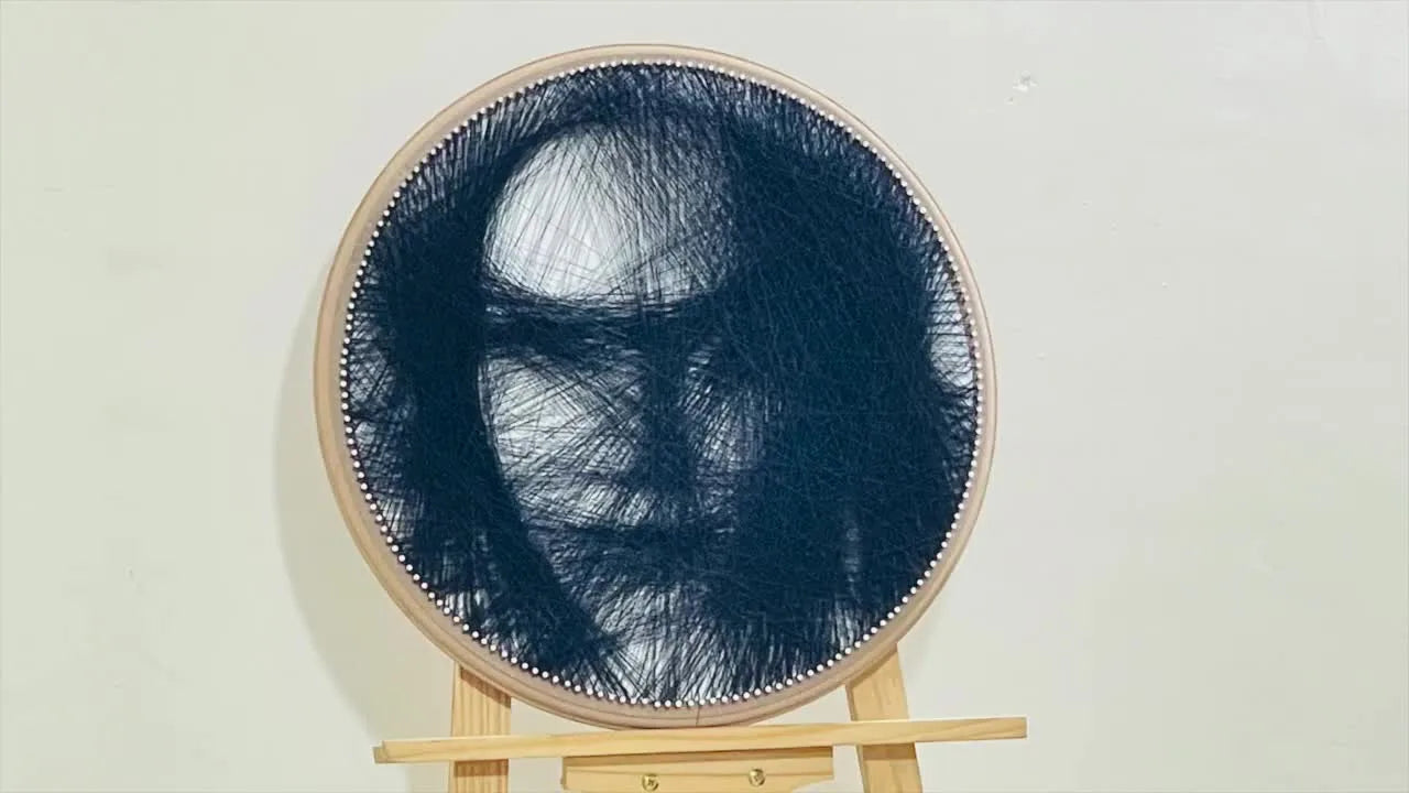 Finished string art portrait of a face, made with black thread on a white background, framed by an oval wooden base.