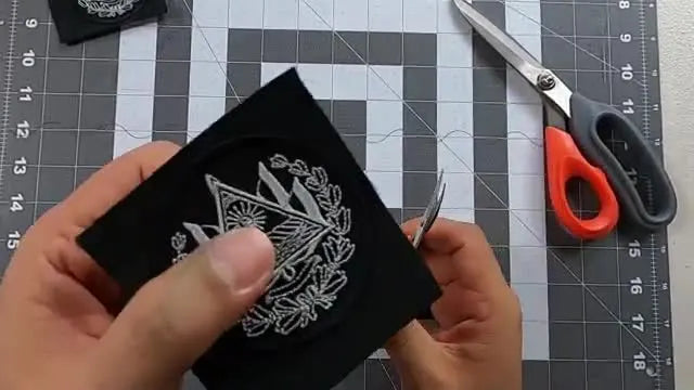 A close-up shows curved embroidery scissors trimming a patch edge cleanly right beside the running stitch for a smooth, professional border.