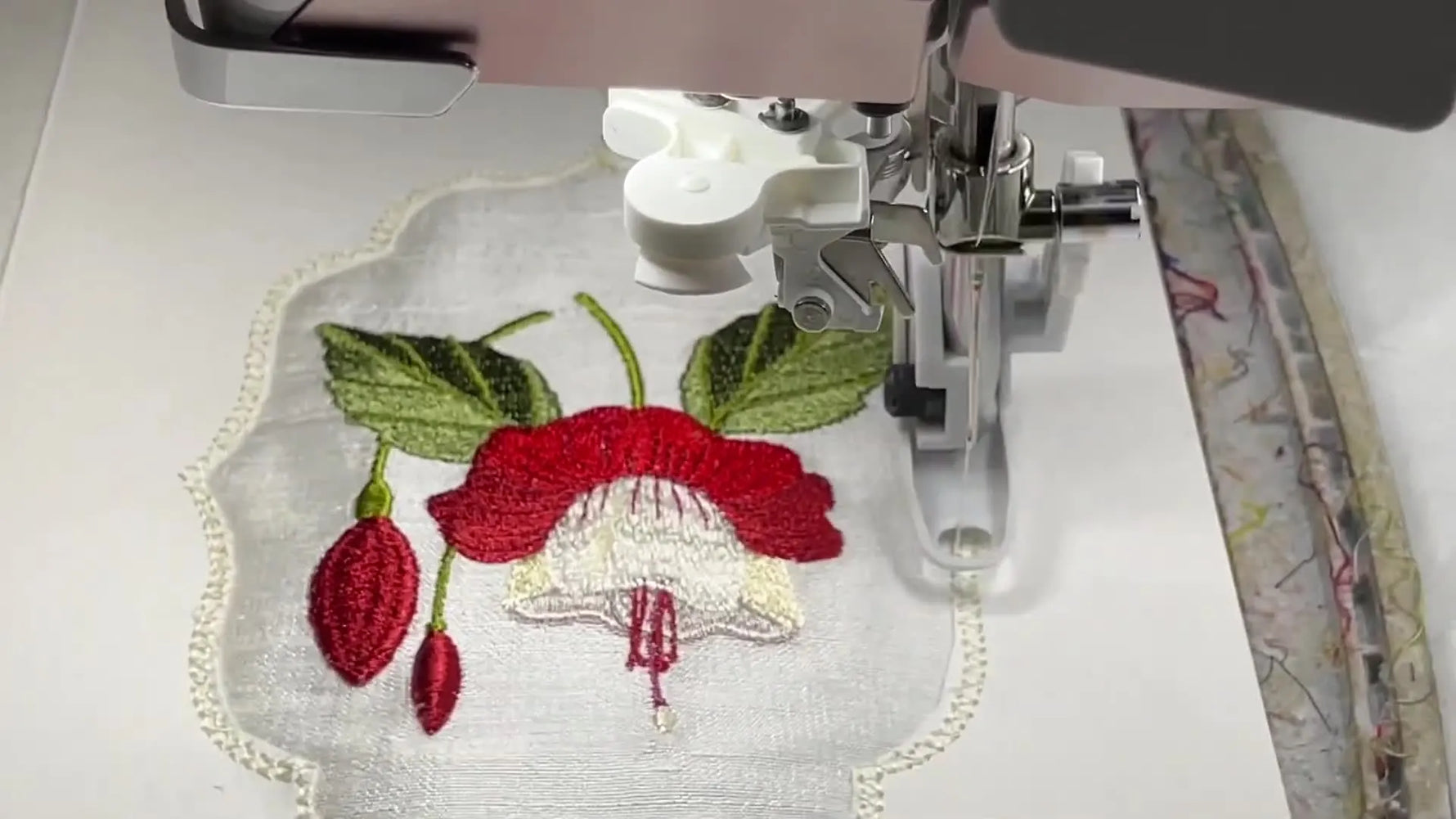 Close-up of the embroidery machine stitching a satin border that locks silk fabric behind a cardstock window for a polished aperture card.