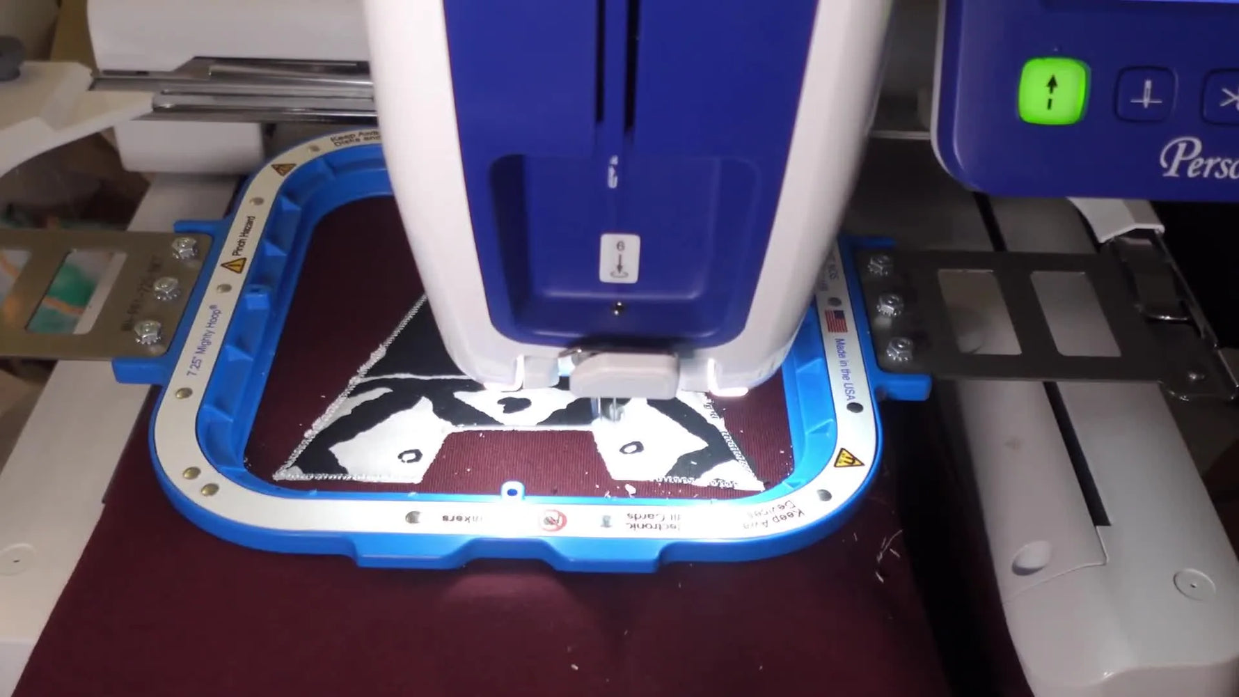 A close-up of the Brother Persona PRS100 stitching the final satin border around an appliqué letter on a sweatshirt held in a magnetic hoop.