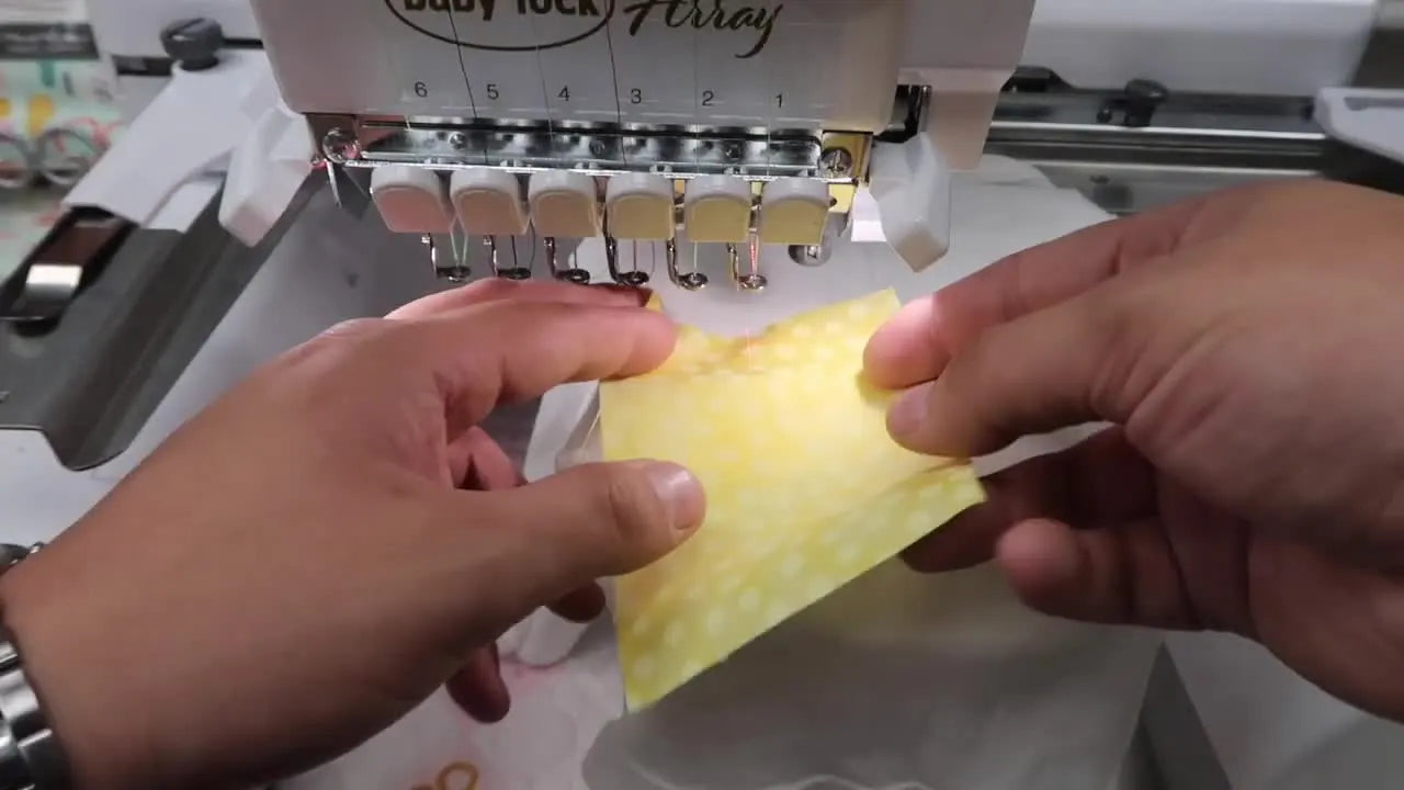 A close-up of the finished pineapple monogram appliqué stitched on a onesie while still mounted on the multi-needle machine arm.
