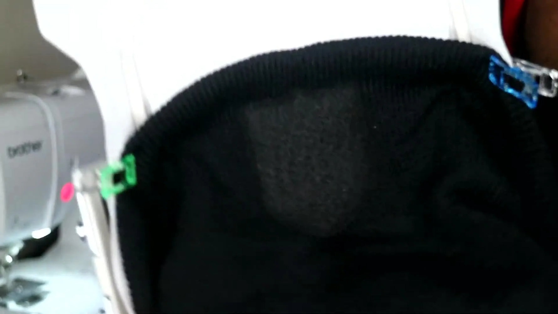 A top-down view of a knit beanie floated on hooped stabilizer with a felt topper stitched down as a clean base layer for the logo.