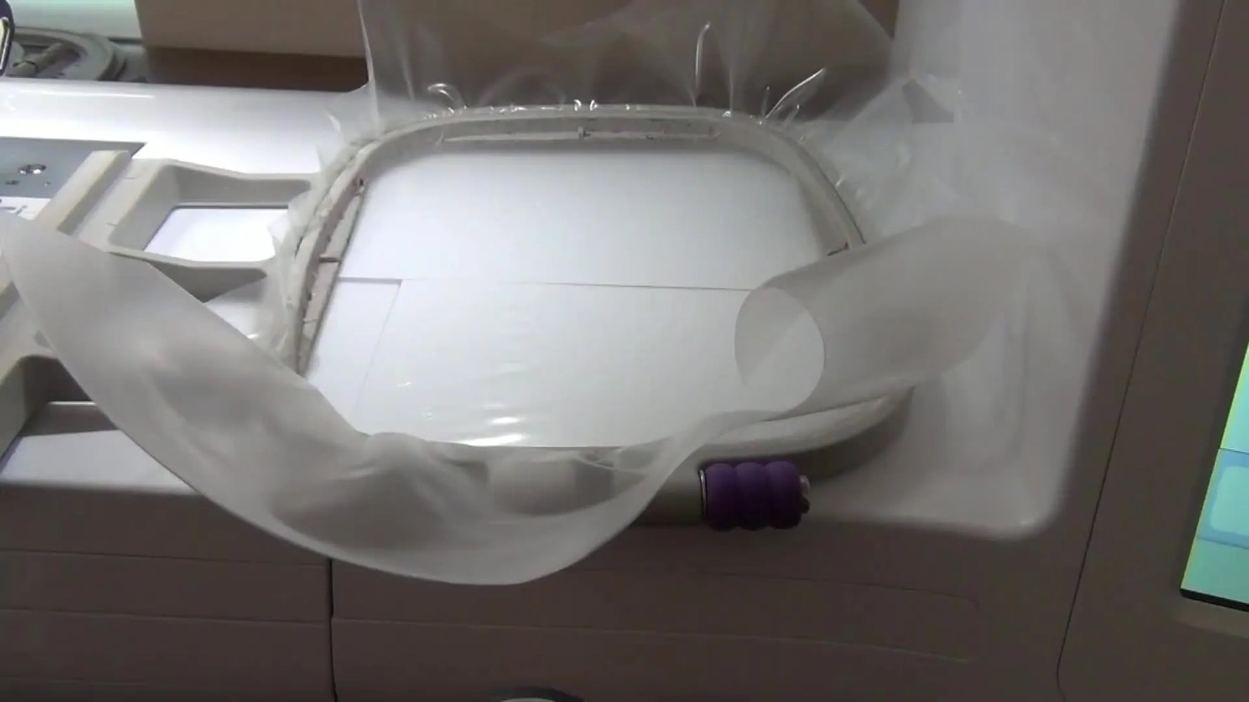 A close-up of a home embroidery machine stitching a freestanding lace earring design onto transparent water-soluble film in a 4x4 hoop.