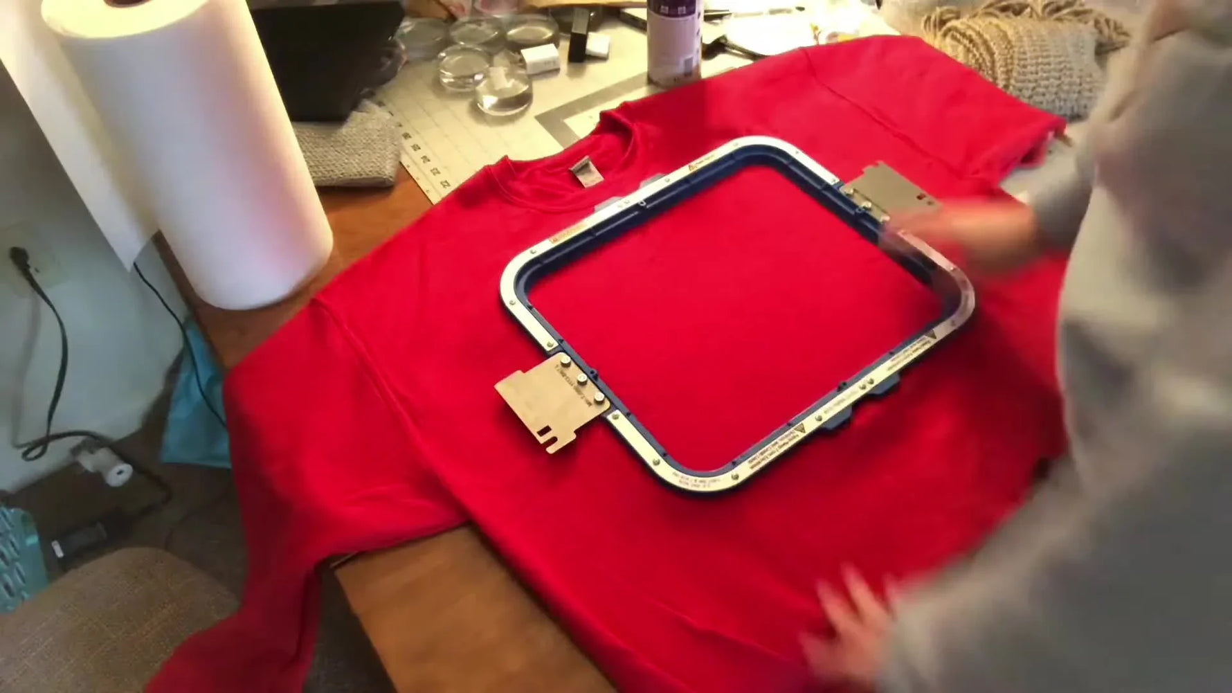 An 11x13 magnetic hoop snapped onto a red sweatshirt, showing a tight, drum-like hooping surface with the warning label facing up.