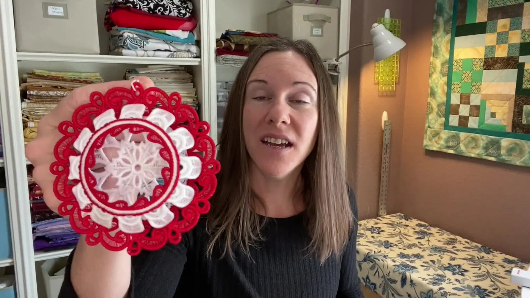 A finished red-and-white freestanding lace ornament is held up close, showing crisp structure and clean open lace areas.