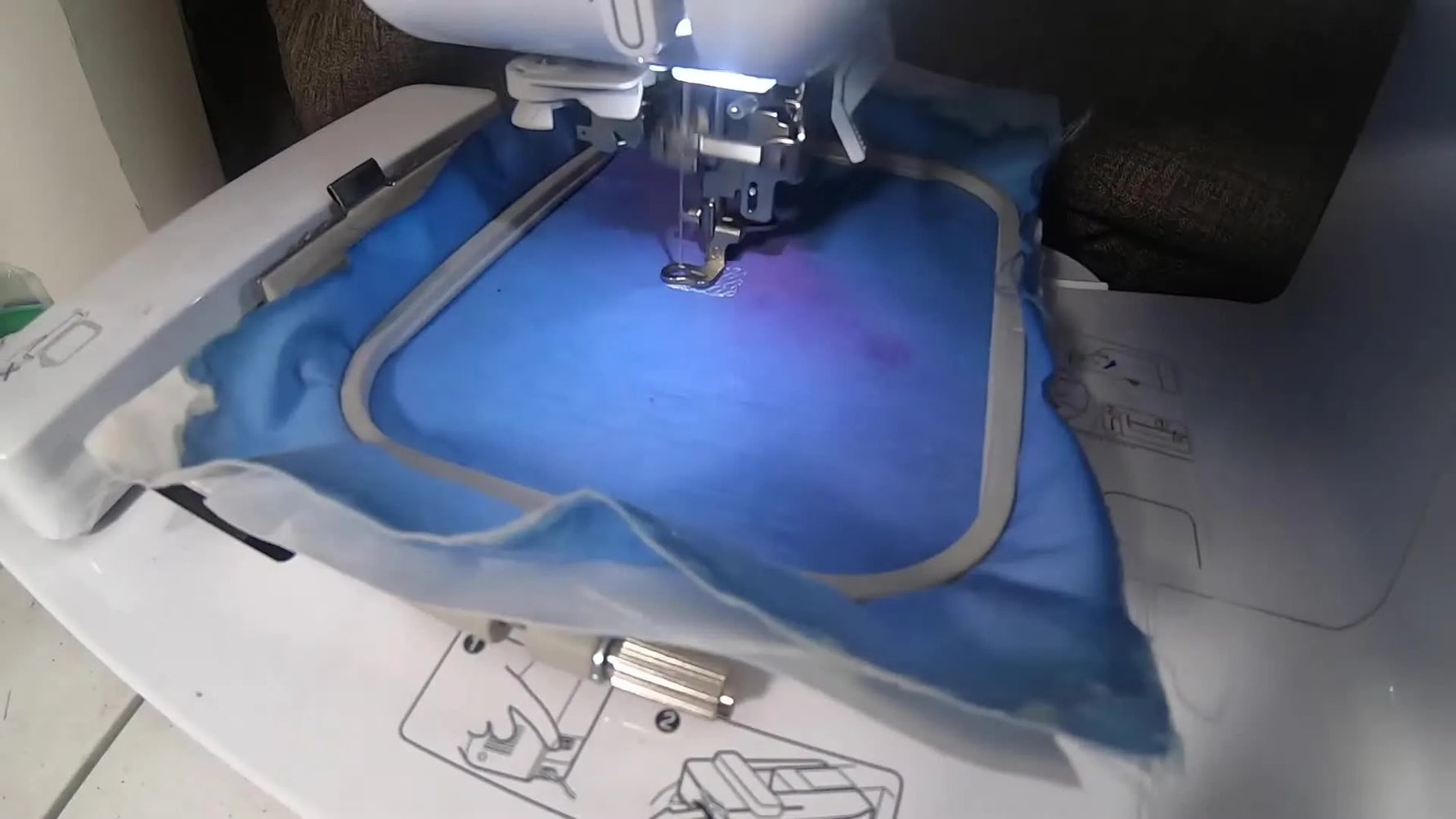 Embroidery machine starting with white thread on blue fabric.