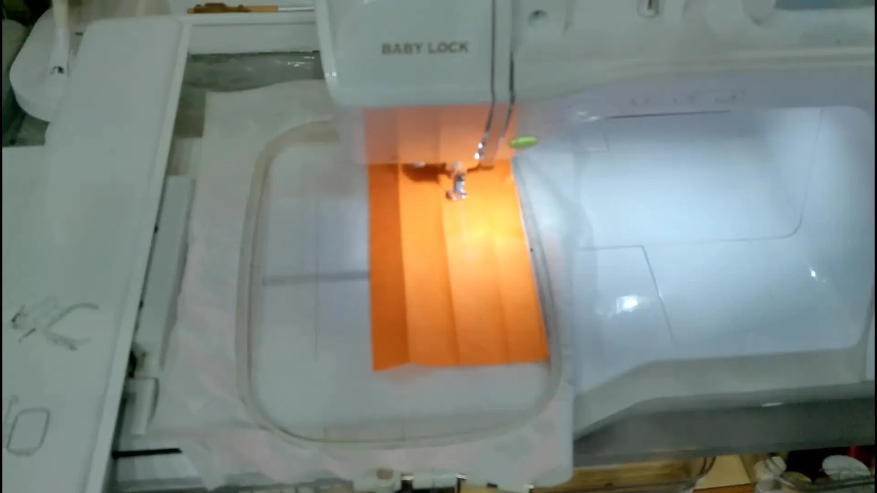 A close-up of a Baby Lock embroidery machine stitching the neon orange “Quack Attack” design onto a narrow wrist strap in the hoop.