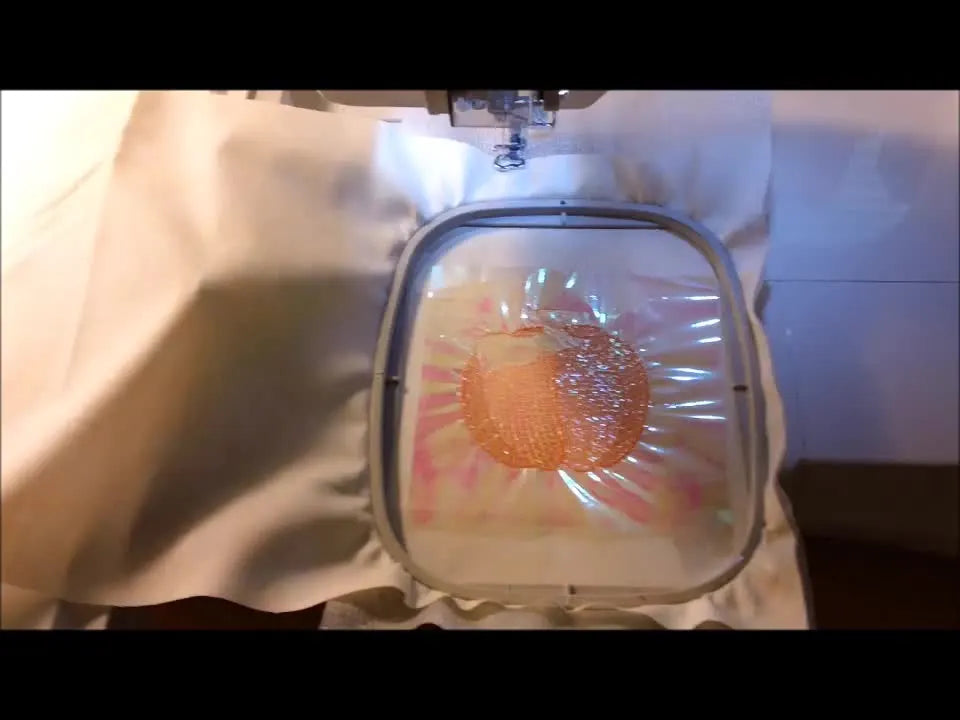A close-up of an embroidery machine stitching an orange fill over opal translucent Mylar, showing the sparkle effect between the stitches.