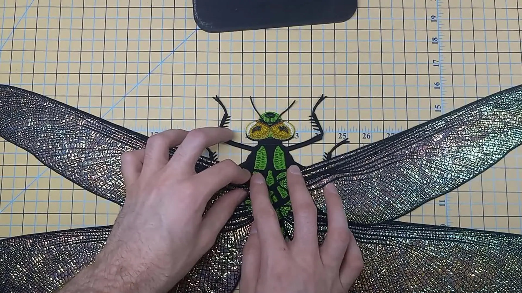An overhead view of the fully assembled giant Meganura dragonfly centered on a gridded cutting mat, showing the final wing angles and tail alignment.
