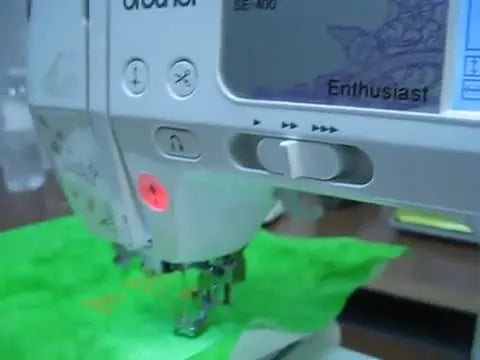 A close-up of the Brother SE400 actively stitching the first letter of a resized word on green felt, showing real-world results of on-screen font resizing and placement.