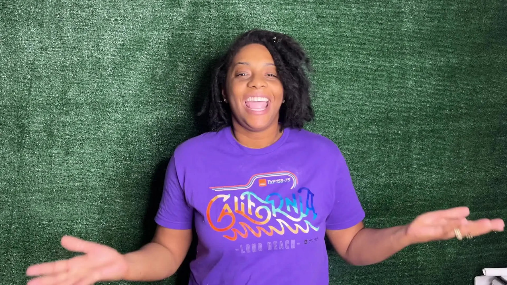 Woman standing in front of green background, gesturing with hands.