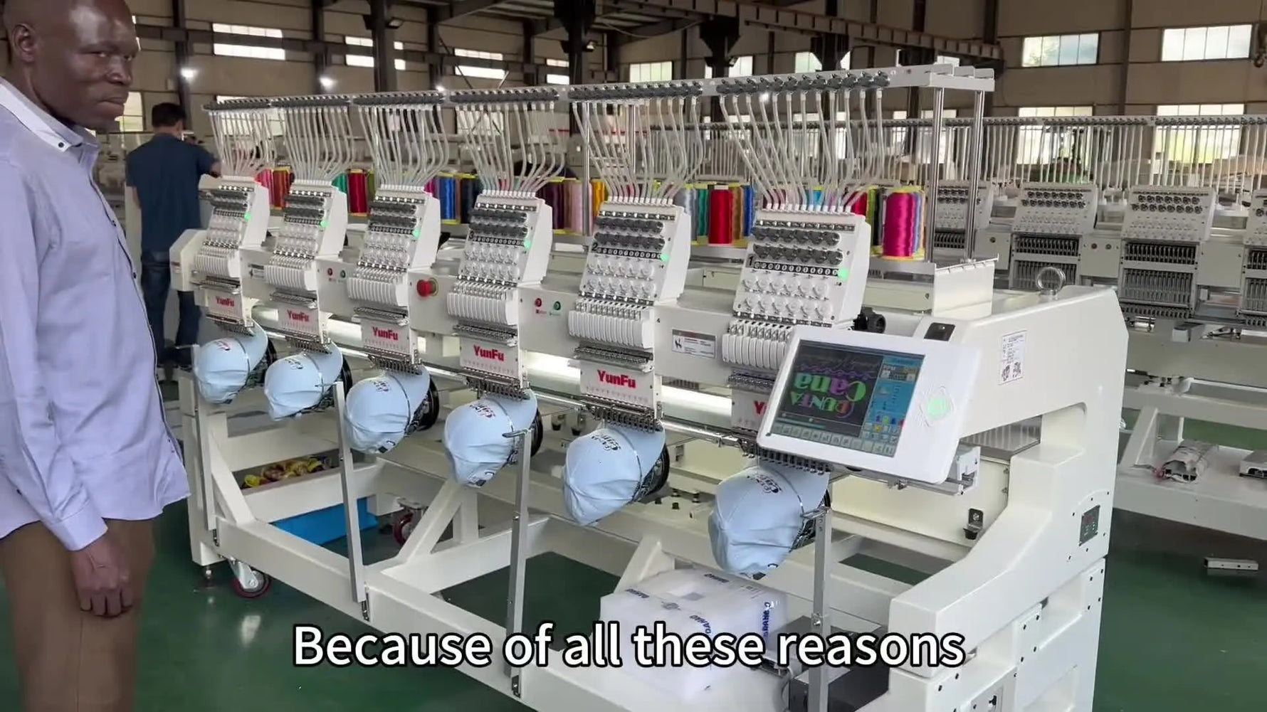 A fully assembled multi-head embroidery machine configured with cap attachments, shown in a wide factory shot.