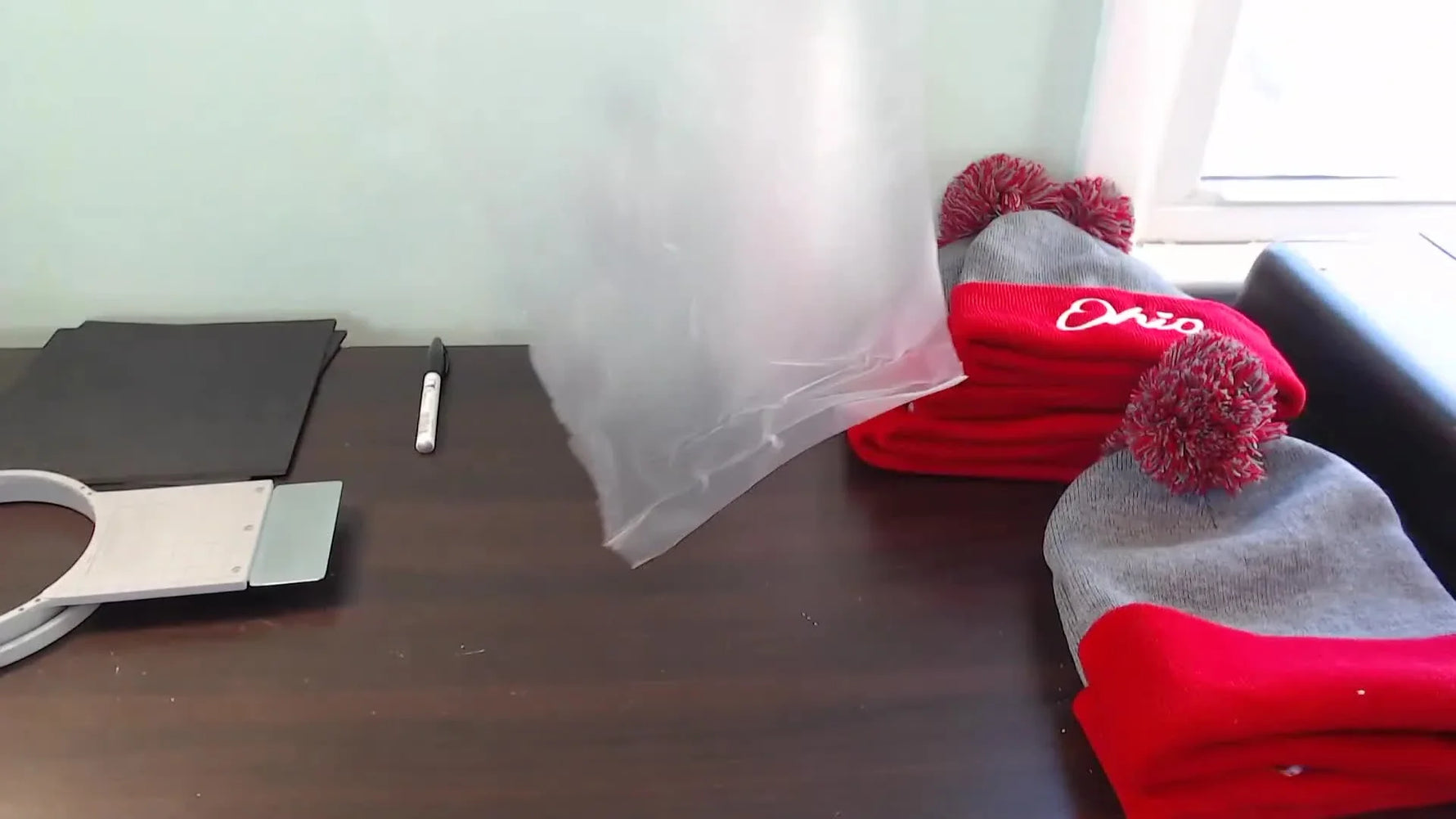 A close-up action shot of a cuffed knit beanie being clamped in the hoop with water-soluble topping on top for crisp, raised stitches.