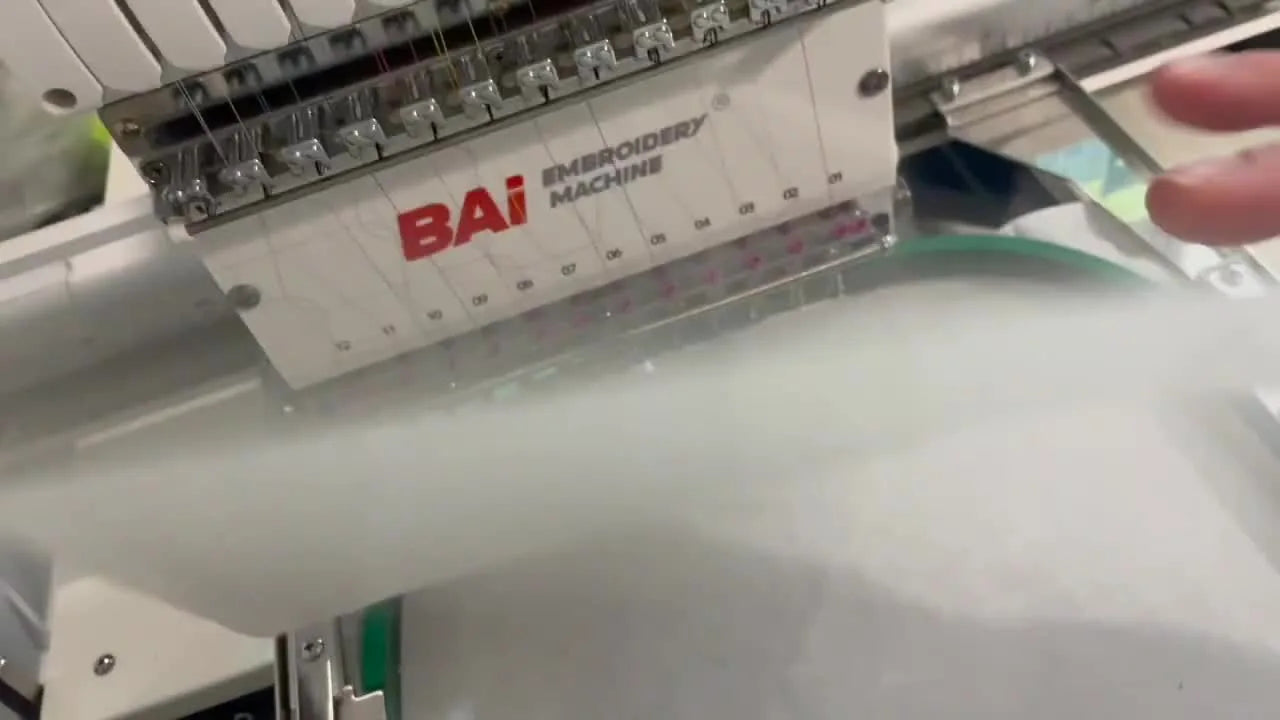 A sheet of duck cloth backed with HeatnBond is floated smoothly over a hooped stabilizer, ready for the tack-down stitch on a multi-needle embroidery machine.