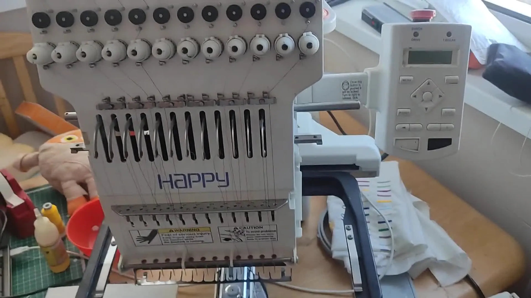 A wide view of the Happy Voyager HCS 1201-30 12-needle embroidery machine set up on a workbench, ready for a full start-to-finish run.