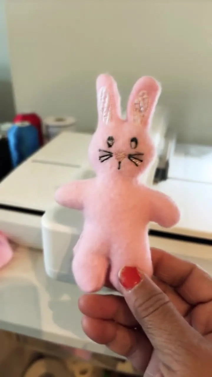 A finished pink fleece ITH stuffed bunny is held up close to the camera, showing crisp facial stitching and plush texture.