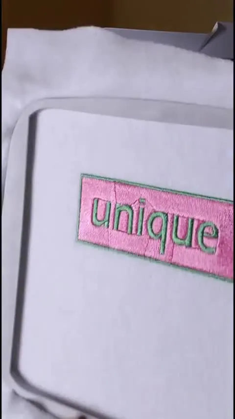 A finished pink-and-green “Unique” box logo patch sits neatly in the Brother SE1900 hoop, ready for trimming and finishing.