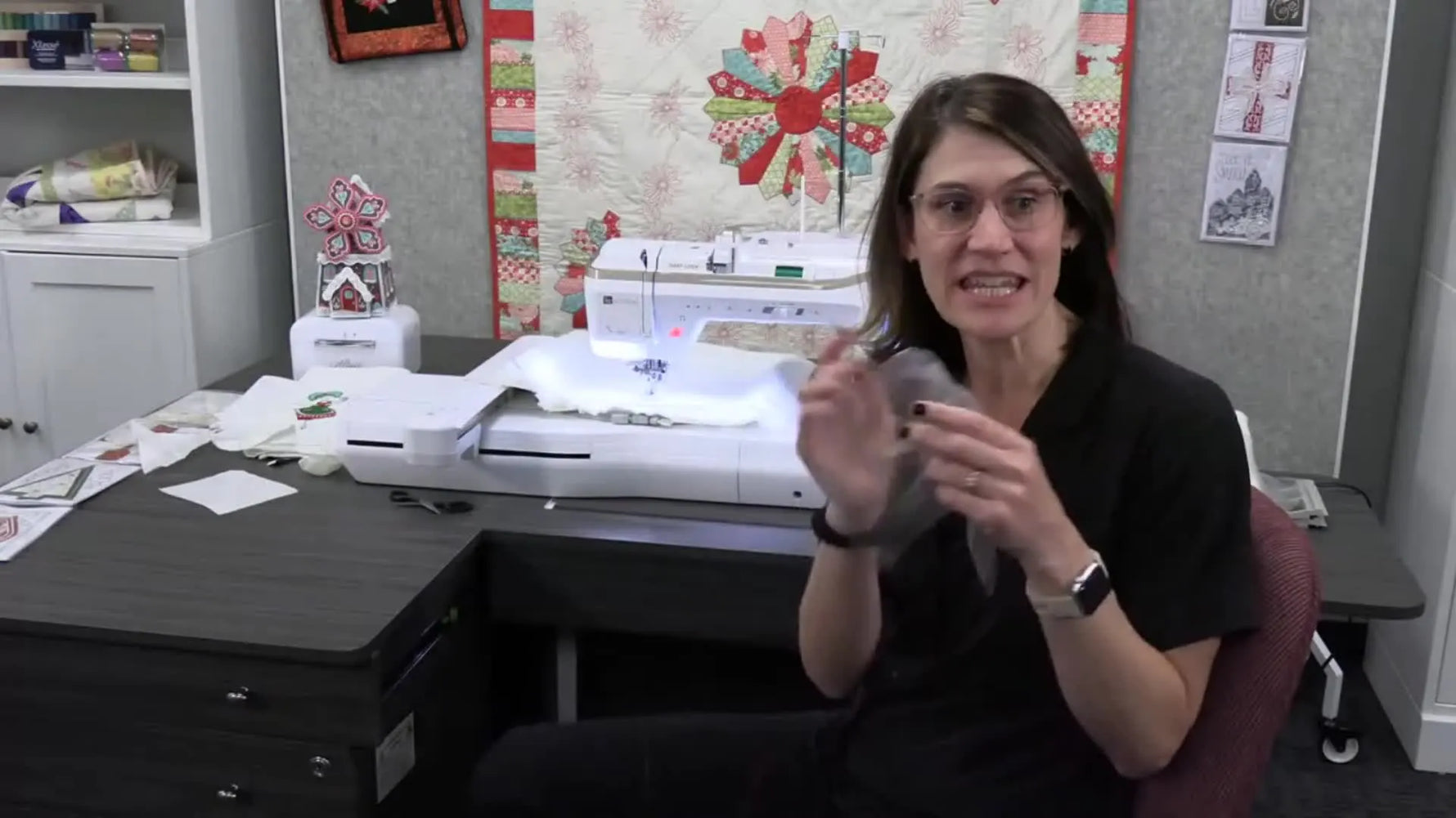 The instructor holds a clear water-soluble topper film beside the embroidery machine, highlighting the key material that keeps towel stitches from sinking into terry loops.