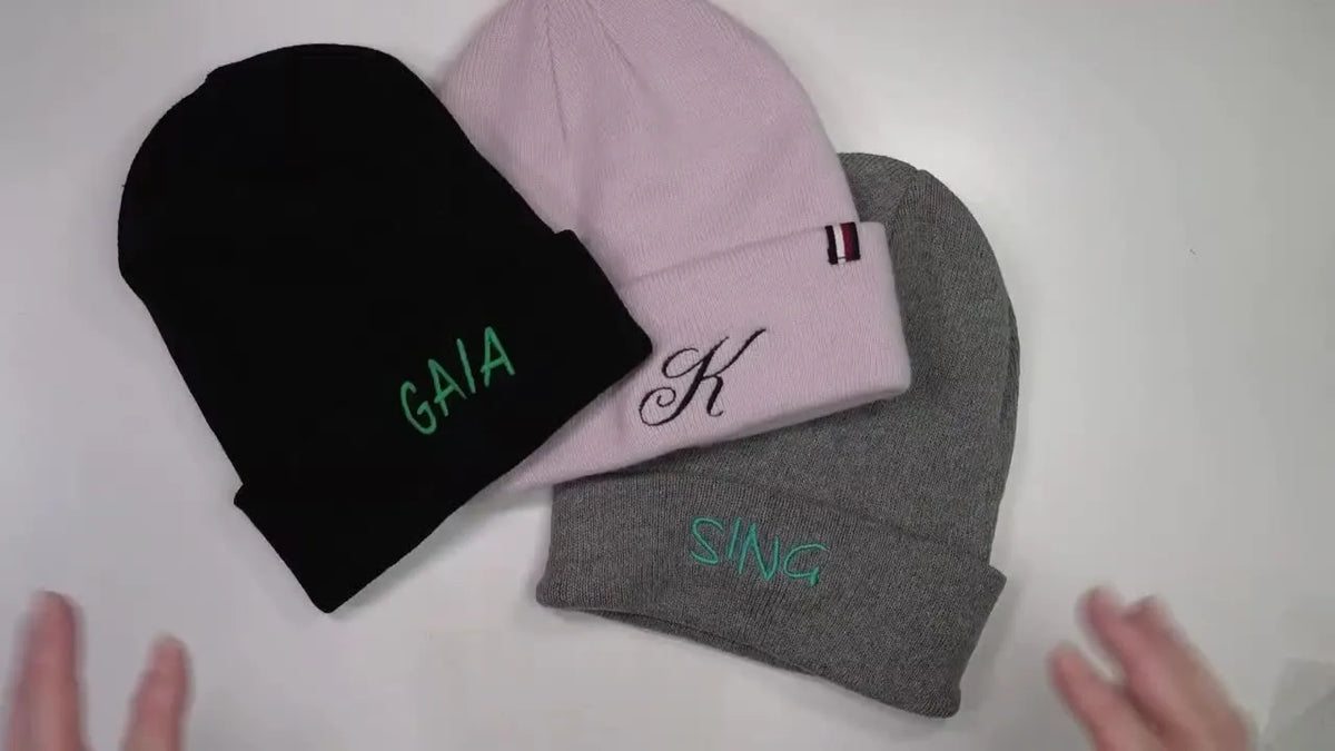 Three embroidered beanies displayed on table.
