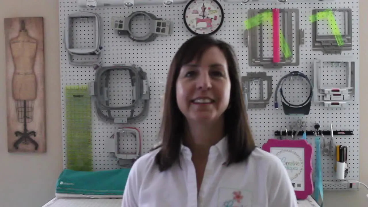 Dawn stands in front of a pegboard wall filled with embroidery hoops, setting the tone for a practical conversation about machines, hooping, and reliable results.