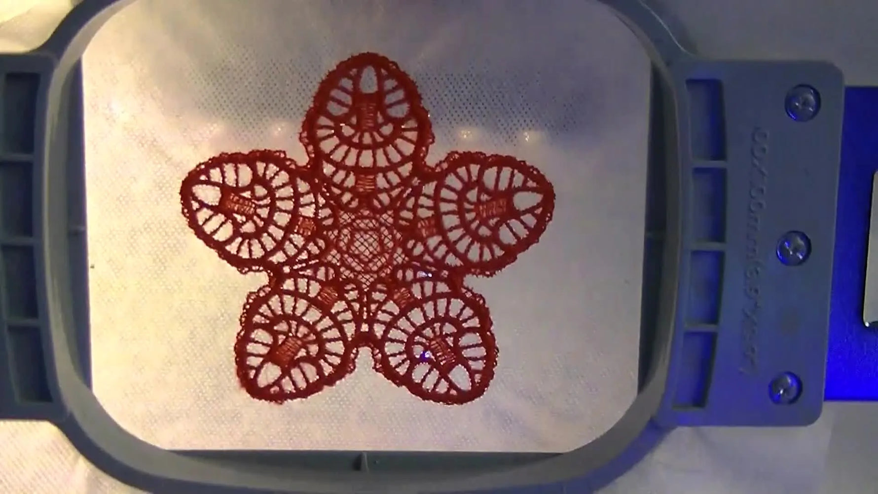 A close-up of a finished bright red freestanding lace snowflake stitched on water-soluble stabilizer while still held in the hoop.