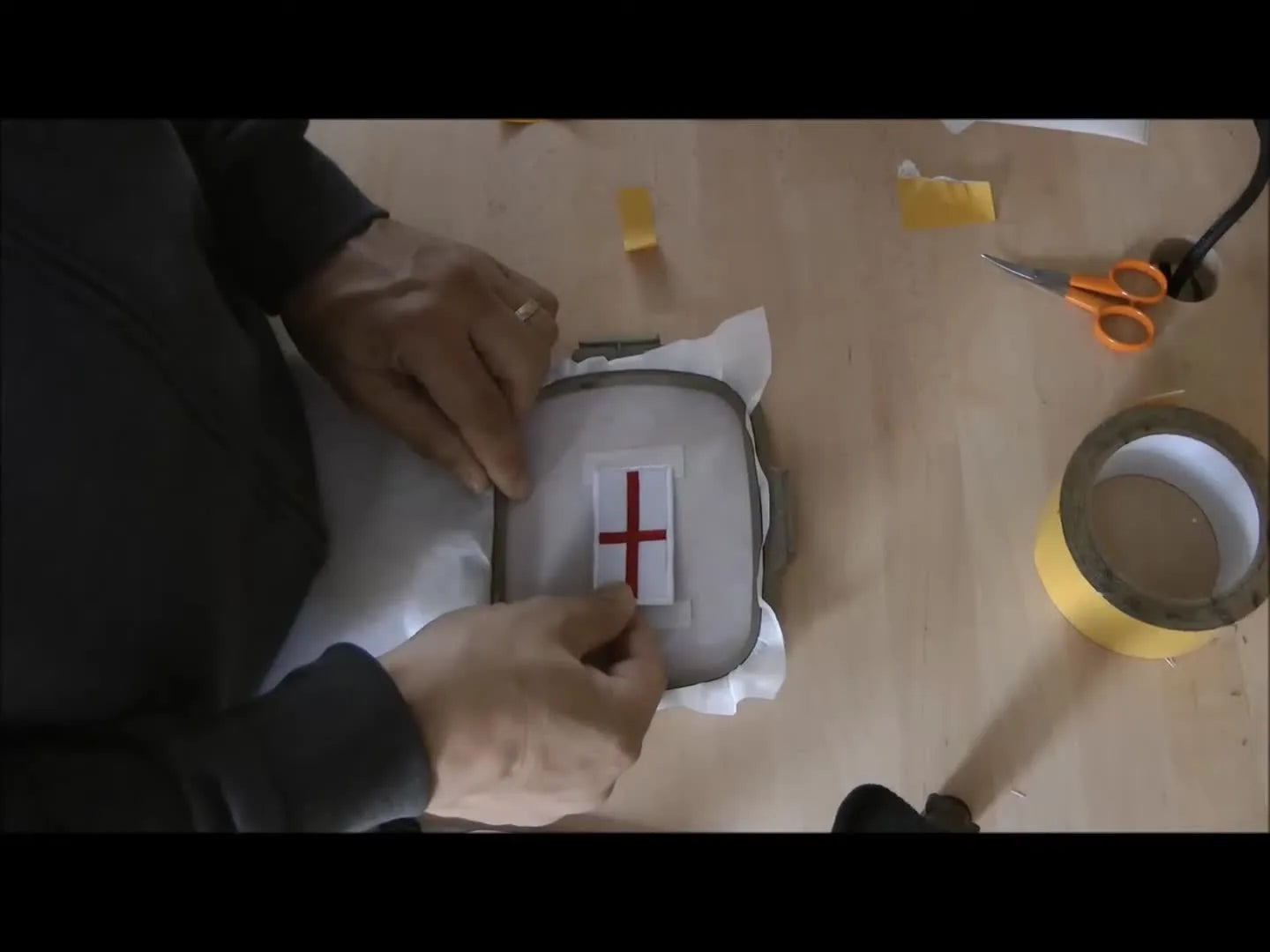 Hands align a St George’s Cross badge onto hooped stabilizer prepared for a floating setup before stitching numbers.
