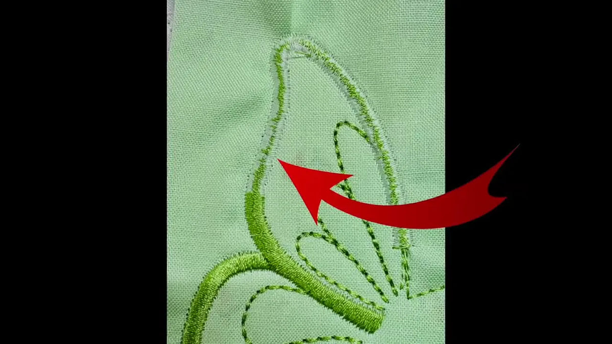 A close-up of green fabric with an embroidered butterfly wing showing messy white bobbin thread.