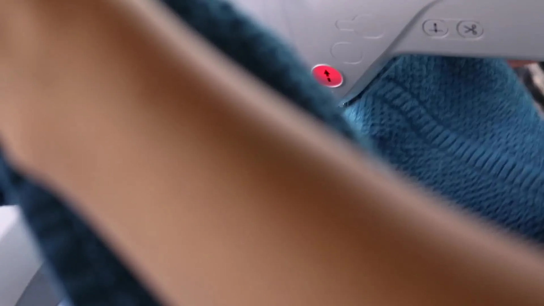 A close-up of the Brother PE800 stitching a white “C” monogram onto a thick teal towel through a water-soluble topper while the towel is floated and pinned.