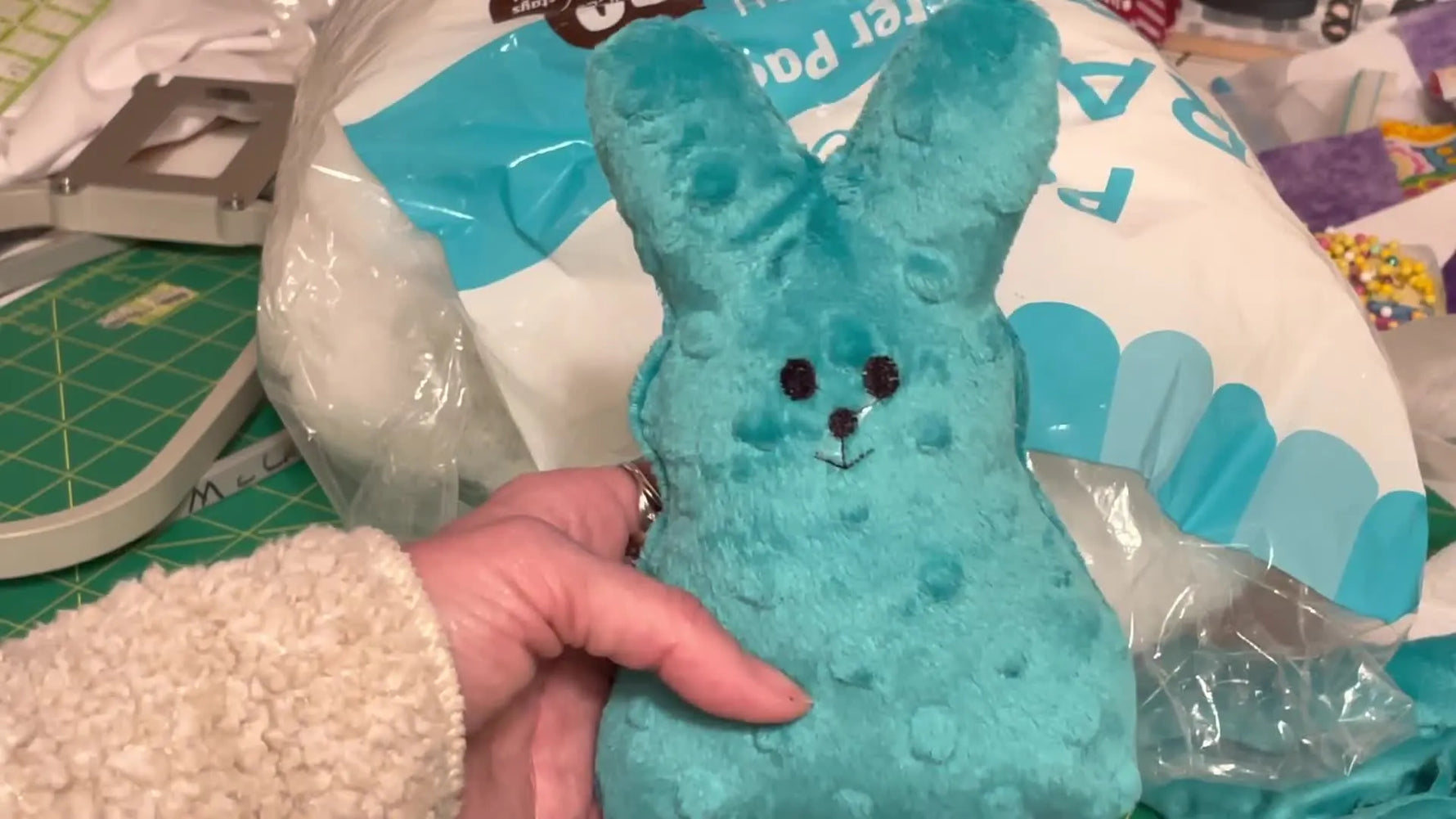A finished teal Minky in-the-hoop bunny softy is held up close, showing the stitched face and plush texture.