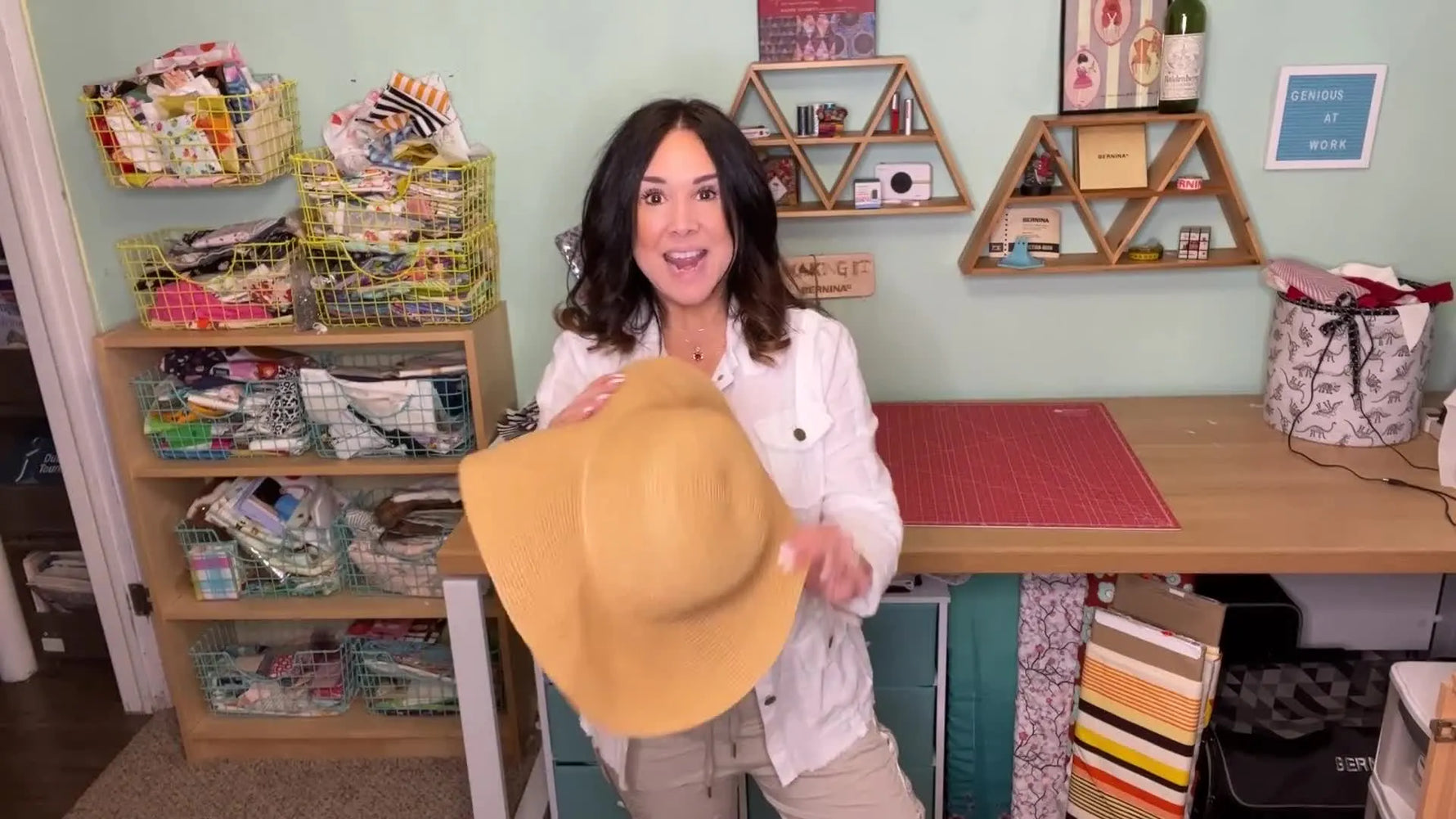A woman in a white shirt smiling and holding a straw sun hat in a craft room.