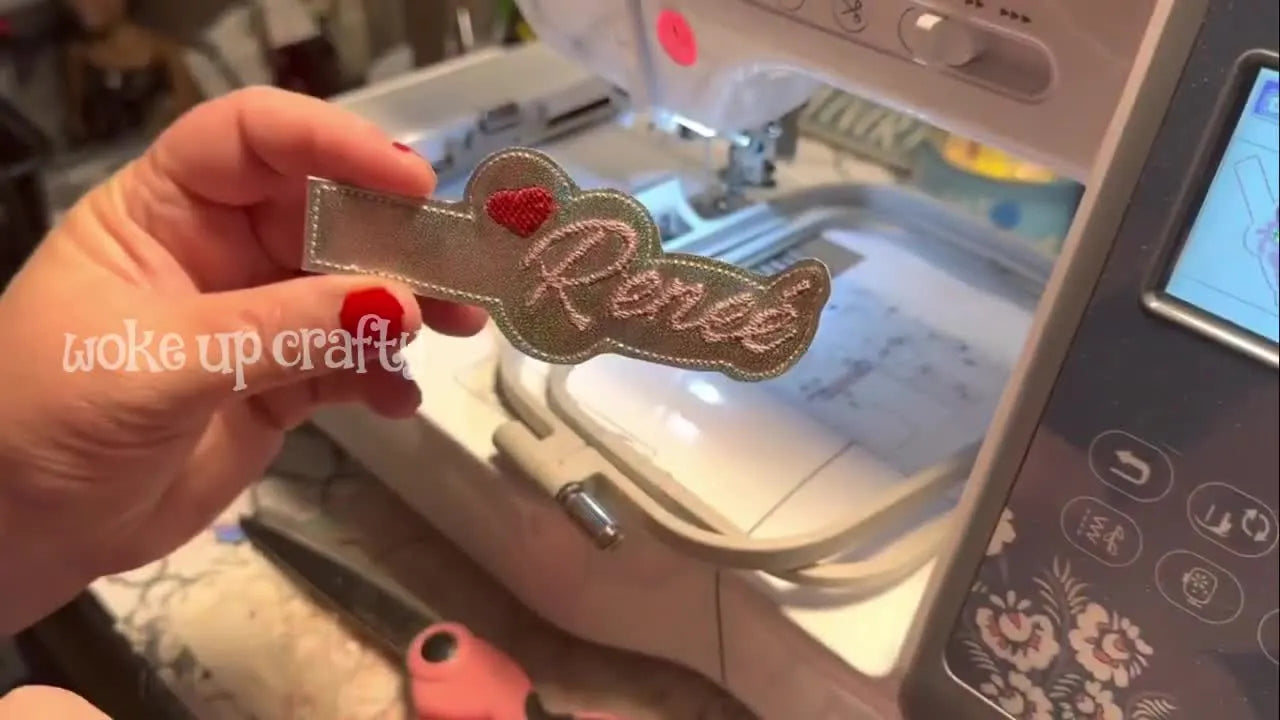 A hand holds the freshly cut holographic vinyl key fob right after stitching, showing the clean outline and finished personalization.