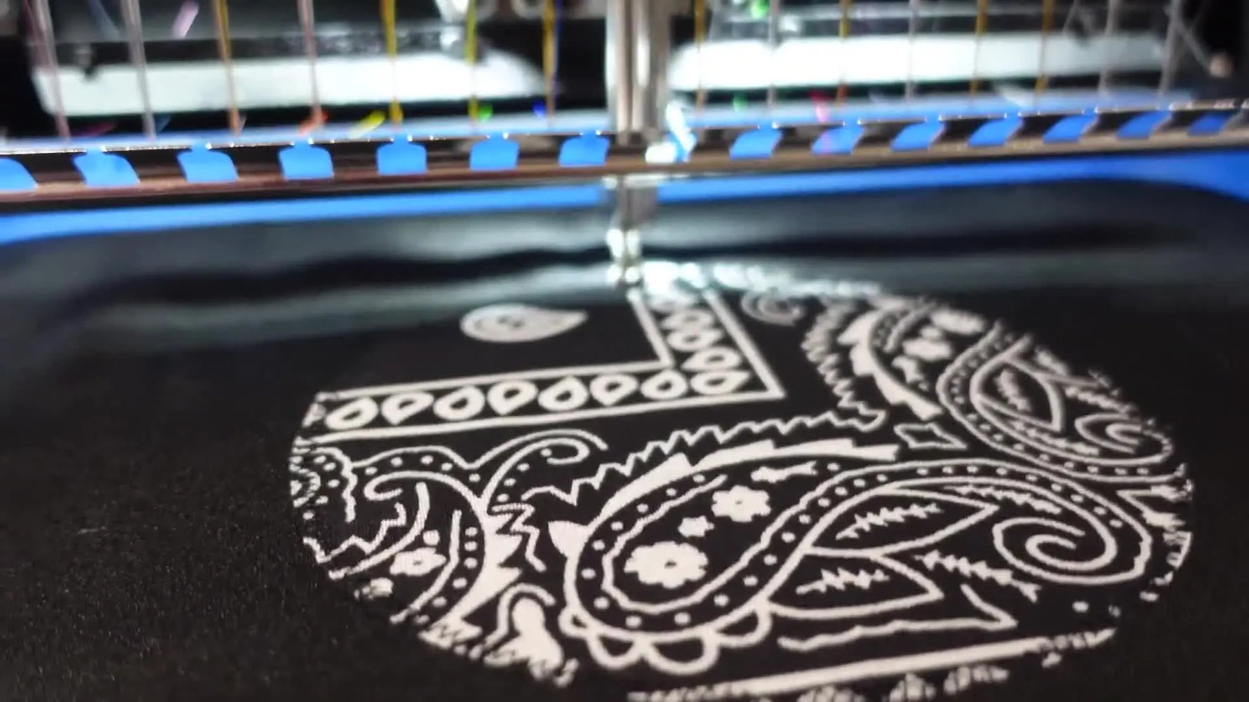 A close-up of the embroidery machine stitching the final satin border and black fill over the bandana appliqué on the apron.