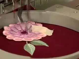 A close-up shows a hand positioning a pre-stitched 3D petal layer on hooped denim right before the machine tacks the center ring to lock everything in place.