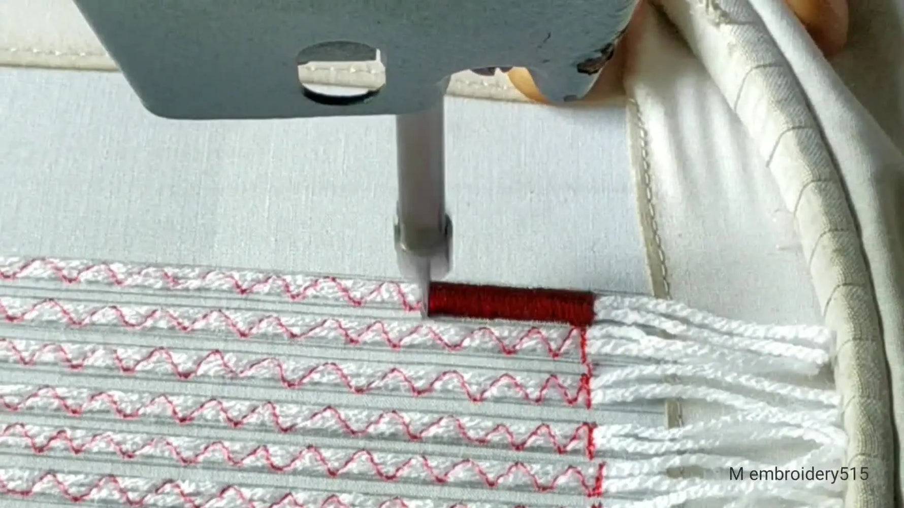 Embroidery machine starts dense fill stitch in dark red over layered white yarn.