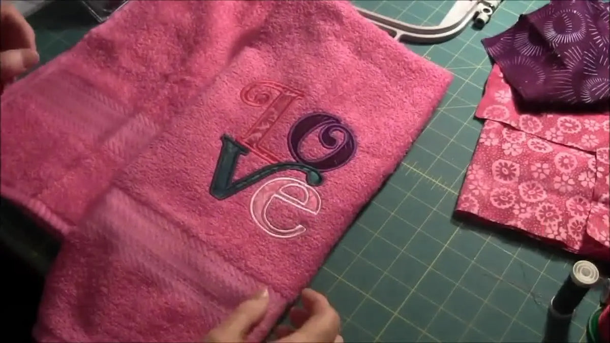 A finished pink towel with a colorful 'LOVE' appliquÃ© embroidery design.